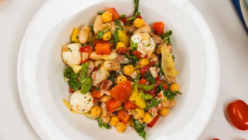Dense chopped bean salad in a white bowl with scattered cherry tomatoes to the side.