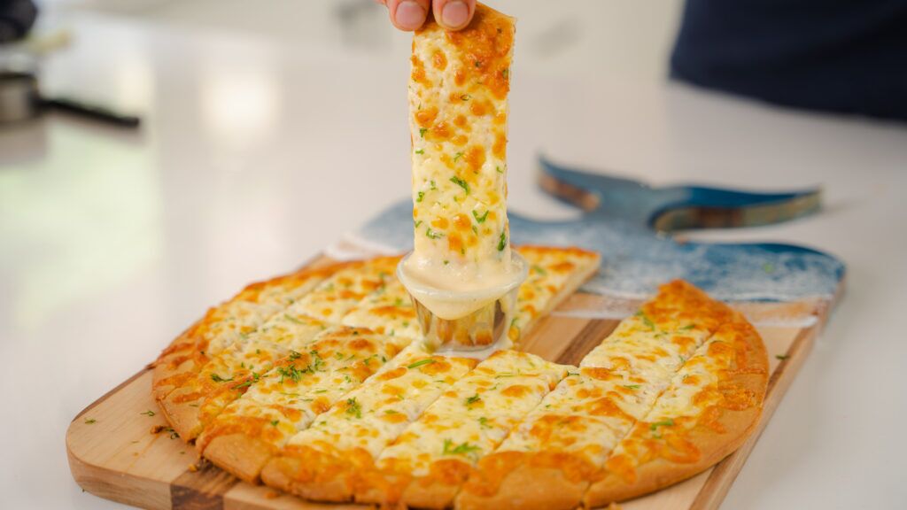 A close up shot of a garlic finger being dipped into Donair Sauce