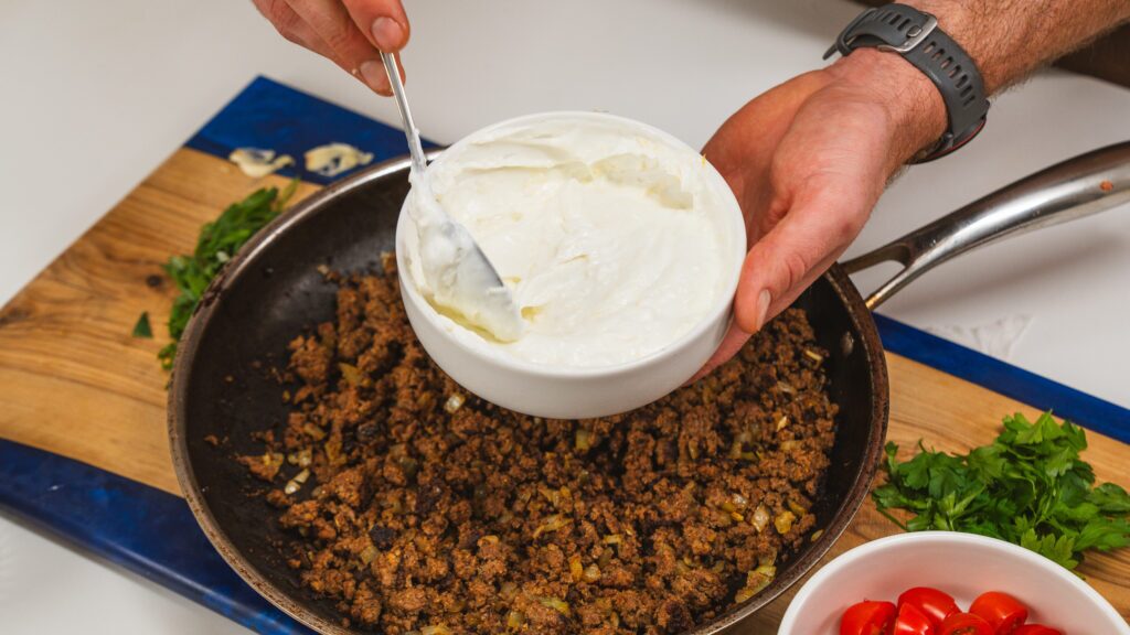 Adding yogurt to ground meet browning in a skillet.