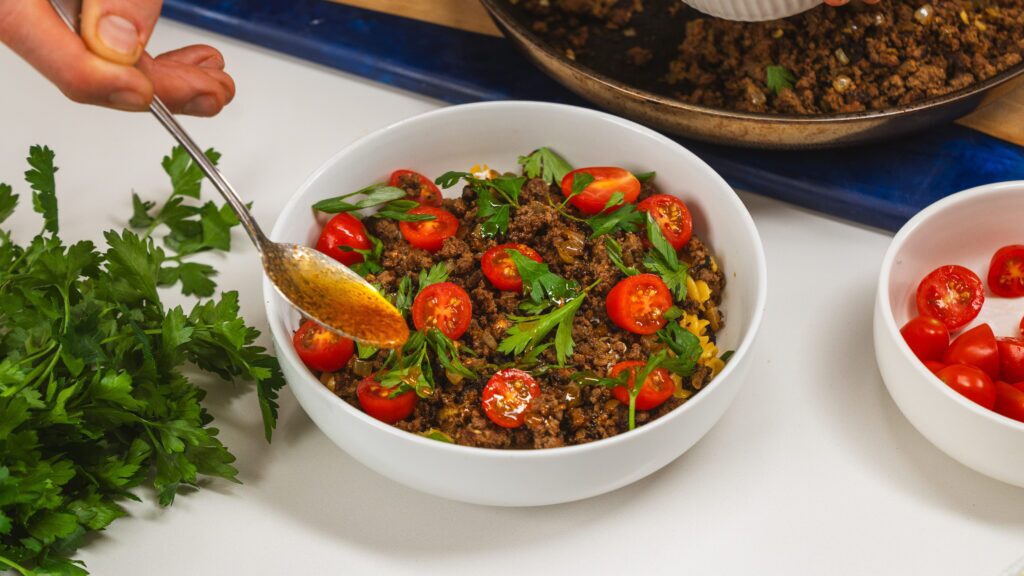 Adding paprika sauce to a bowl of Anna Paul's viral Turkish pasta.