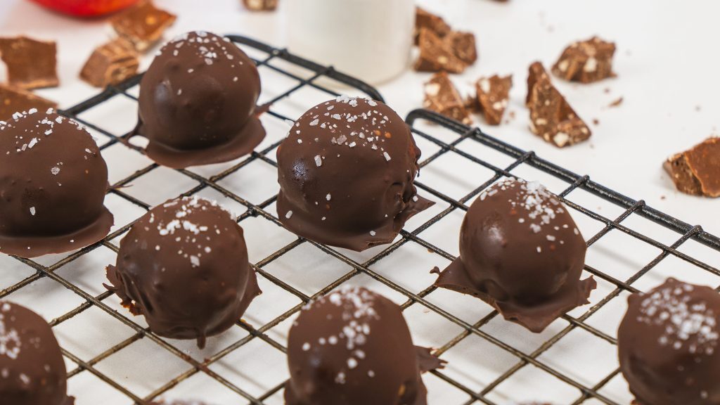 Peanut butter protein balls sitting on a wire wrack. They are covered in dark chocolate and sea salt.