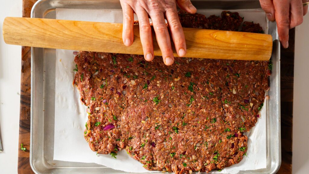 Rolling seasoned ground beef onto a piece of parchment to make beef kebabs.