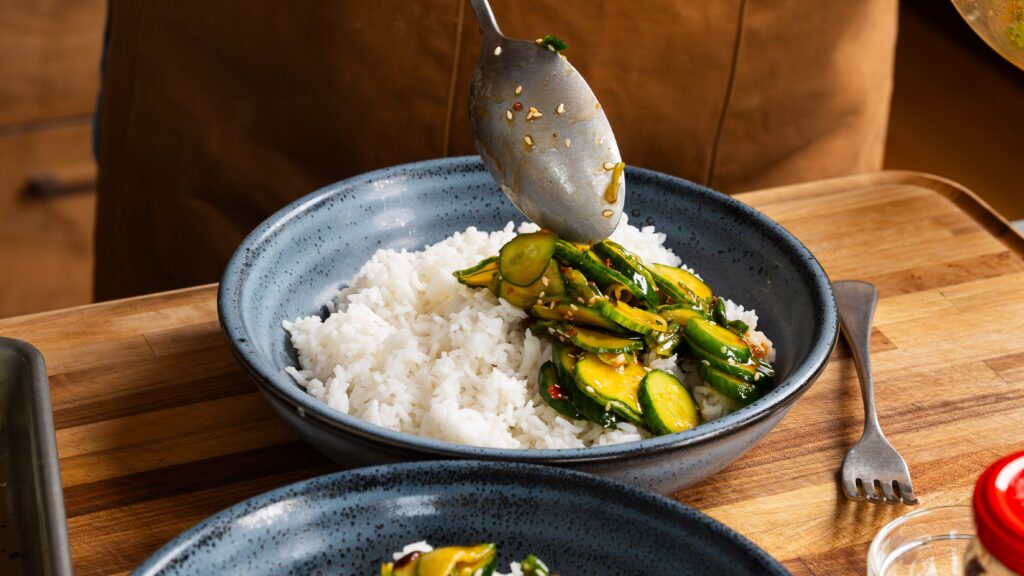 Spooning cucumber salad over rice to make a delicious brown sugar salmon dish.