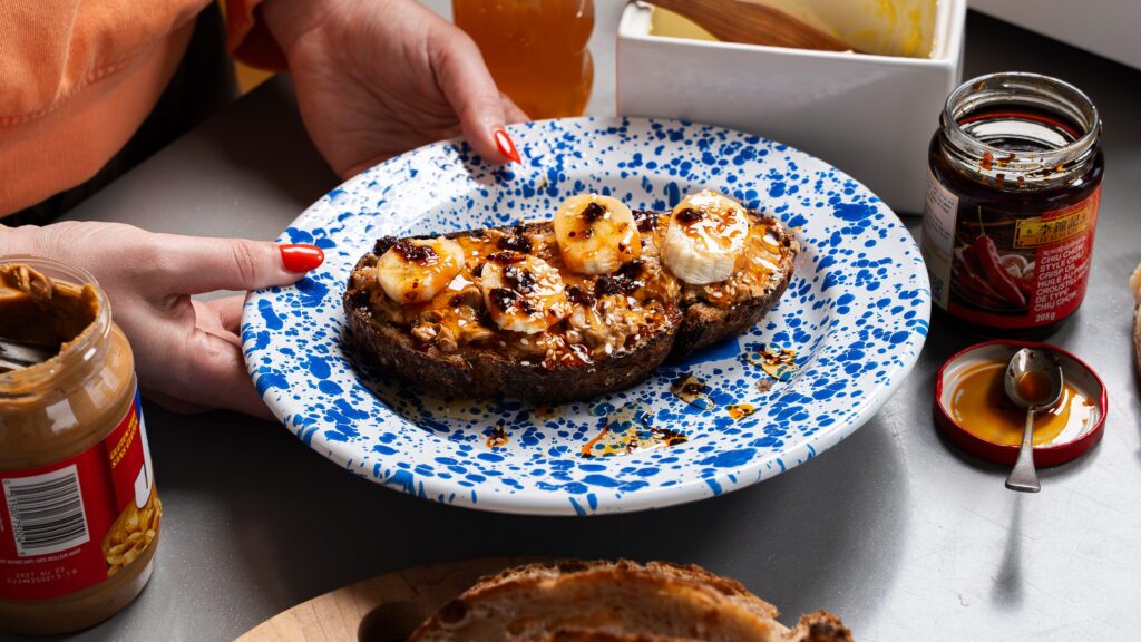 A peanut butter on toast recipe with banana, chili crisp and honey on a plate.