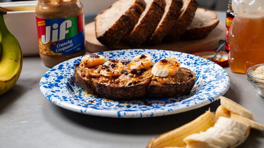 A peanut butter on toast recipe with banana, chili crisp and honey on a plate.