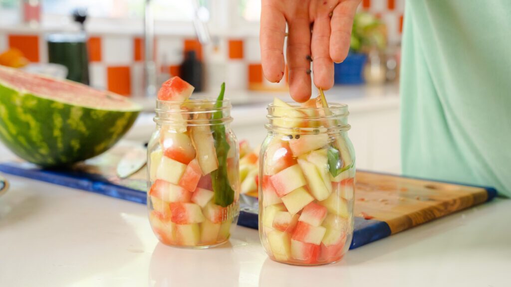 Adding spices to jars for a pickled watermelon rind recipe.