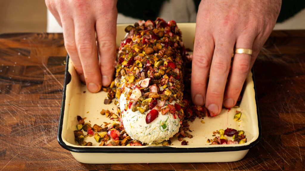 Coating a cheese log in chopped pistachios and fresh cranberries.
