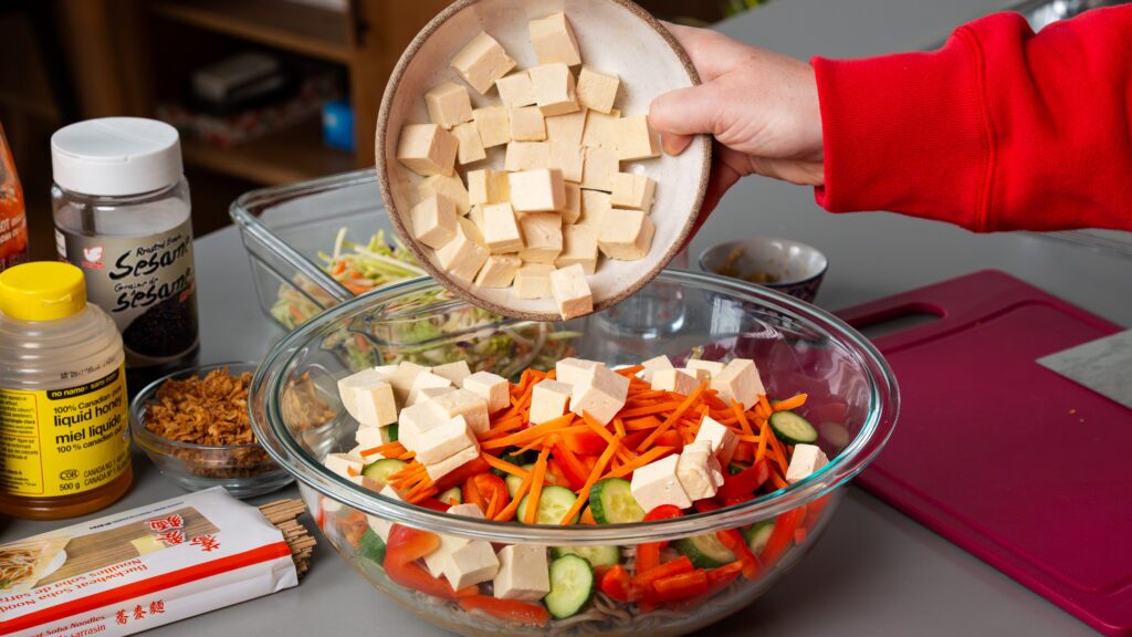 Adding tofu to a soba noodle salad bowl.