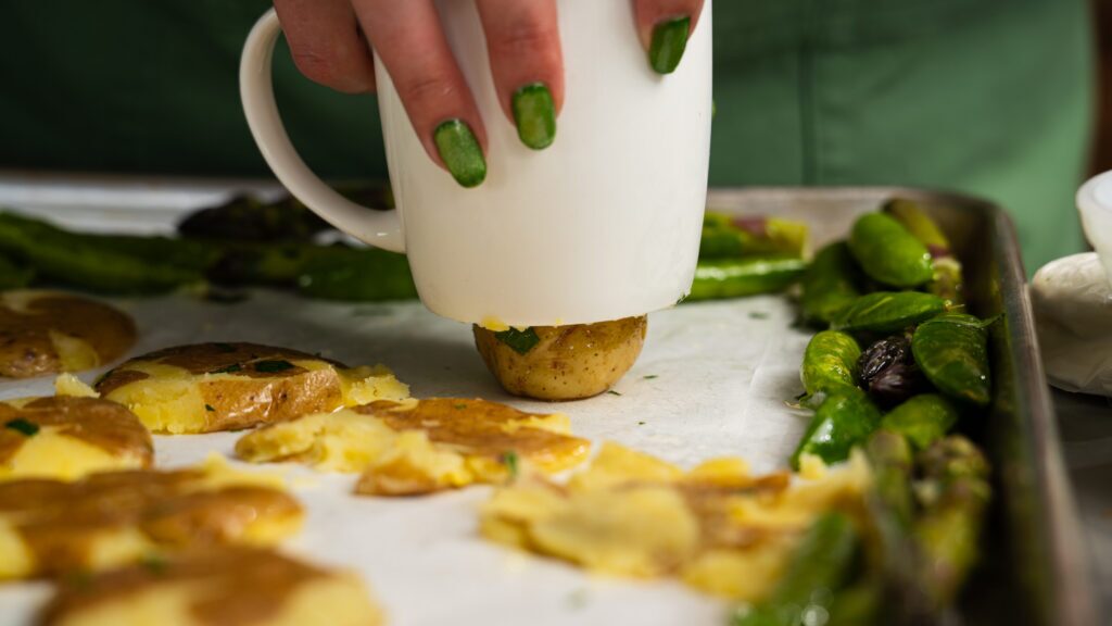 Smashing the potatoes with the bottom of a mug for this sheet pan chicken and potatoes recipe.