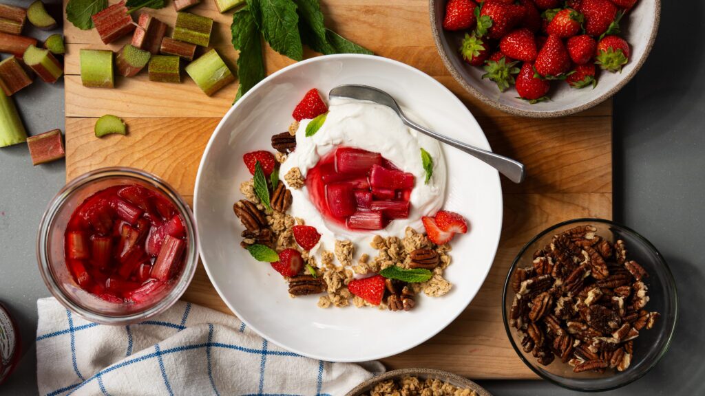 Roasted rhubarb with yogurt and granola in a white bowl.