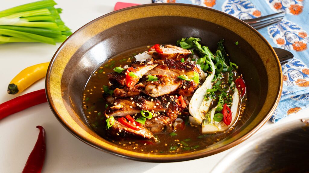 Brothy chicken and rice in a bowl with wok chop and other vegetables.