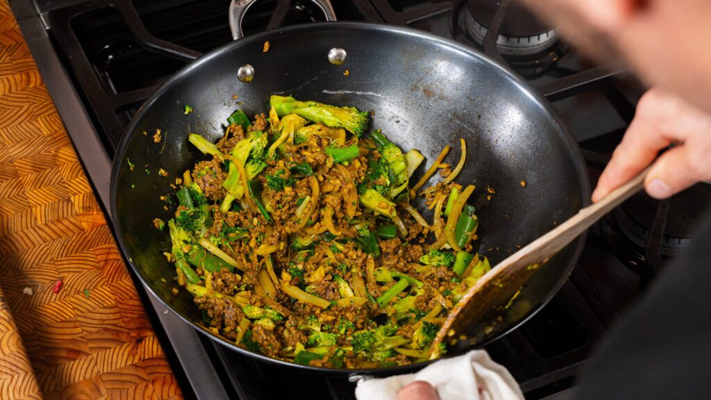 Beef and broccoli stir fry in a pan, coated in glossy sauce with Jamaican curry powder.