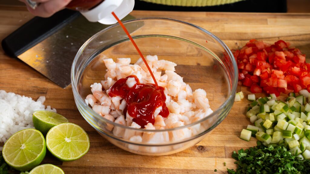 Adding ketchup to cooked shrimp for a delicious shrimp cocktail recipe.