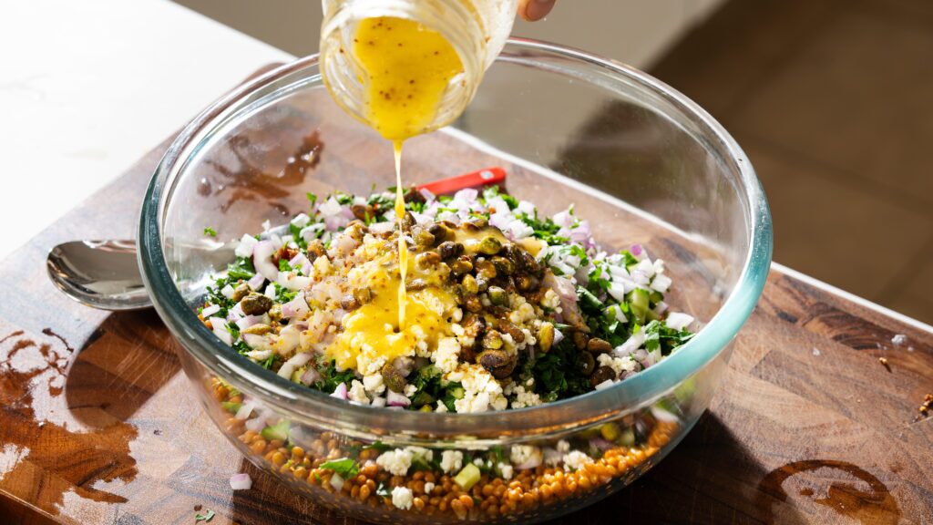 Drizzling salad dressing into a bowl of lentil salad with feta.