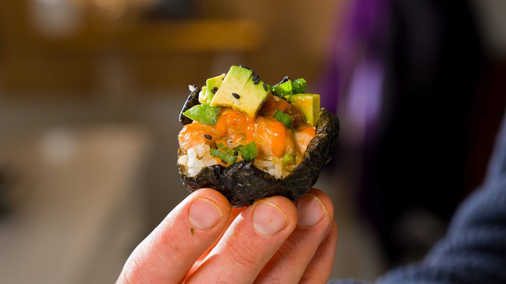 Someone holding a spicy salmon sushi cup in their hand.