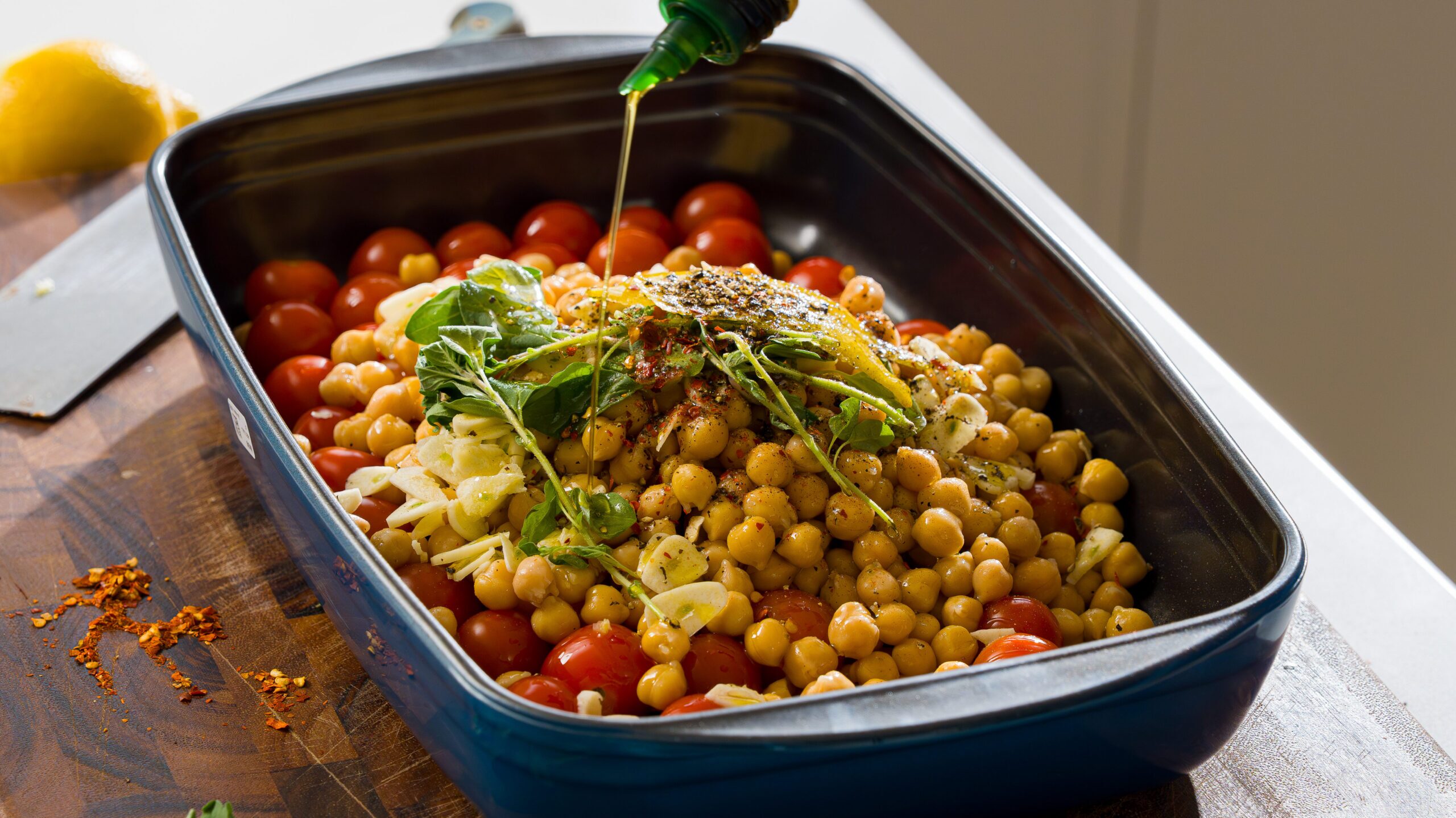 Adding olive oil to a pan of roasted chickpeas with tomato and feta.