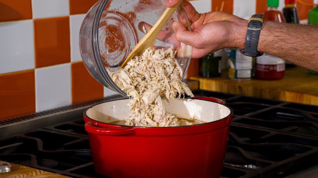 Adding shredded chicken to a pot for a delicious white bean chili recipe.