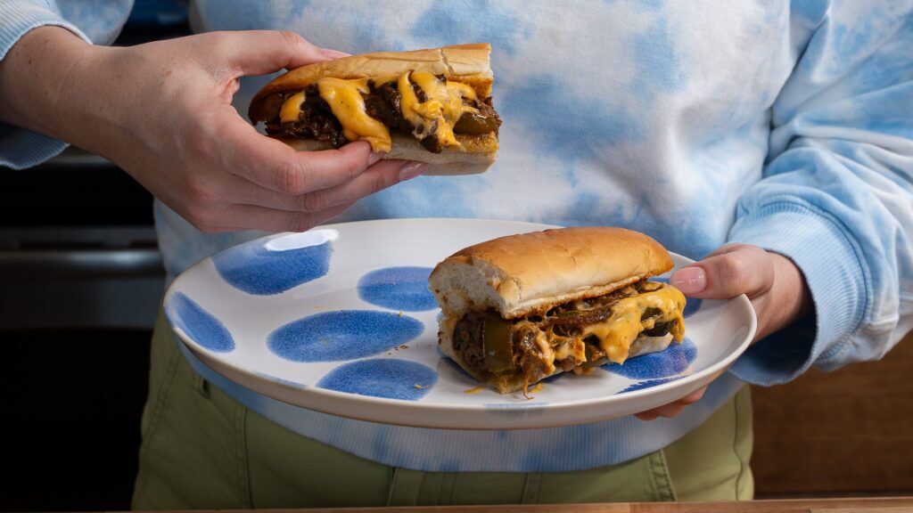 Holding a cheesesteak sandwich in hand.