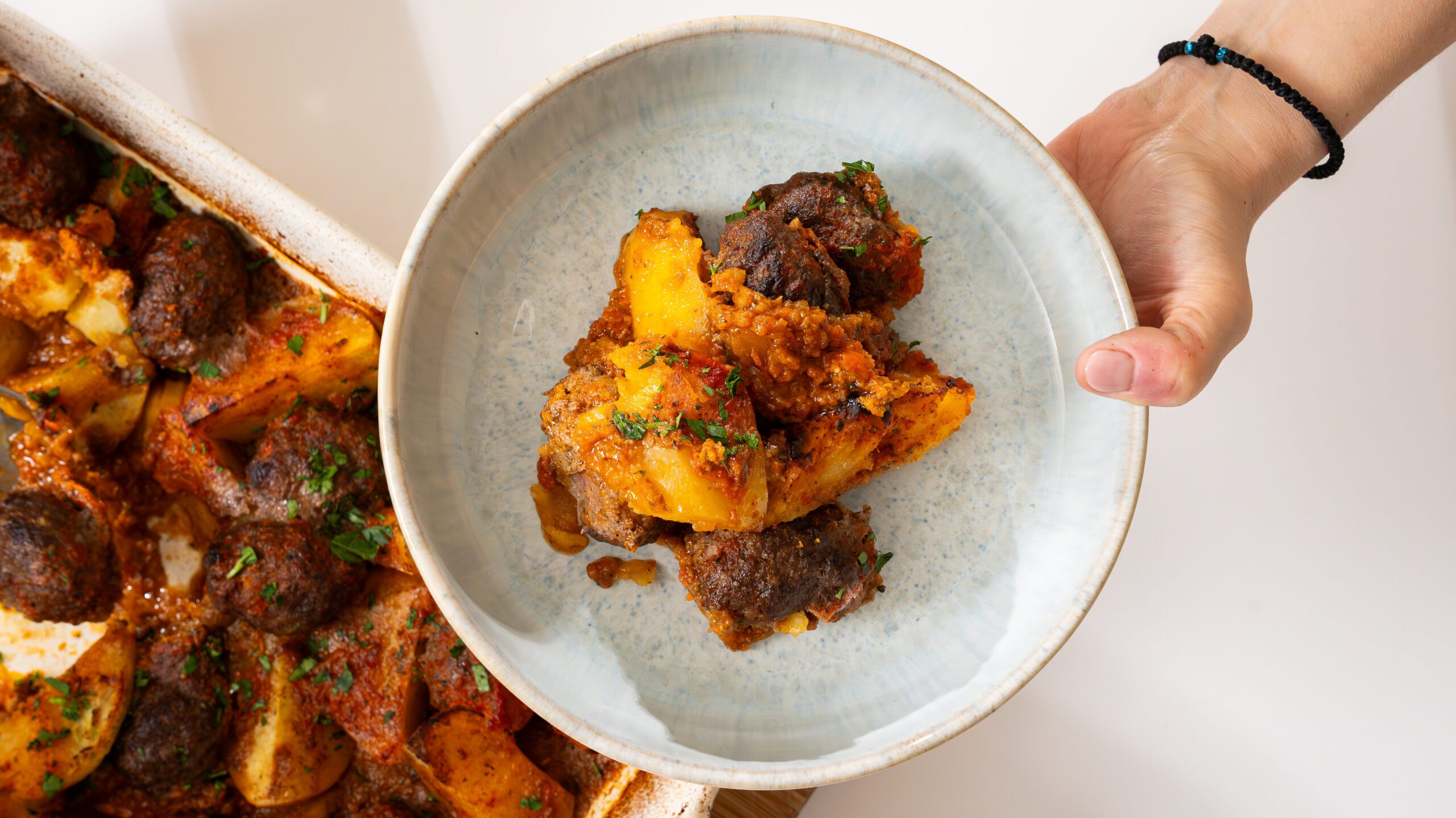 Plating up Greek meatballs and potatoes with an herbed tomato sauce.