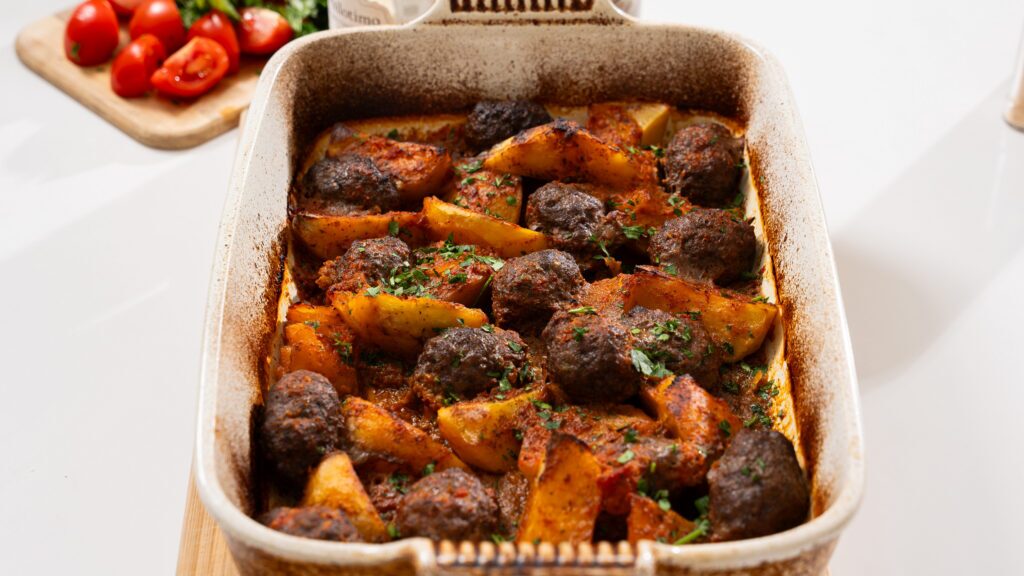 Gluten free baked keftedes and potatoes in a casserole dish.