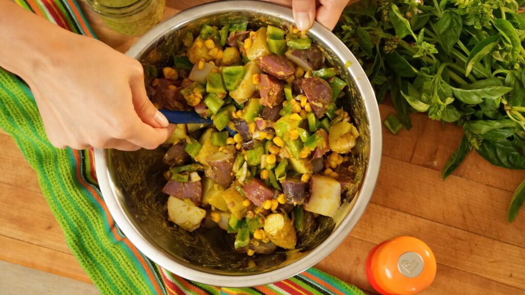 Mixing ip a bowl of corn salad with potato and jalapeño.