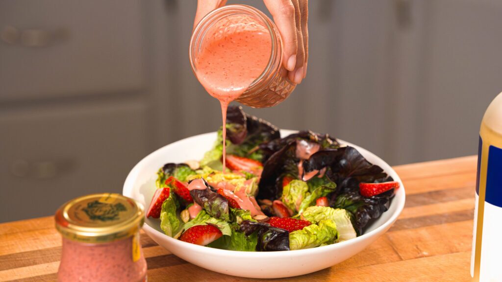 Pouring strawberry vinaigrette over a green salad.