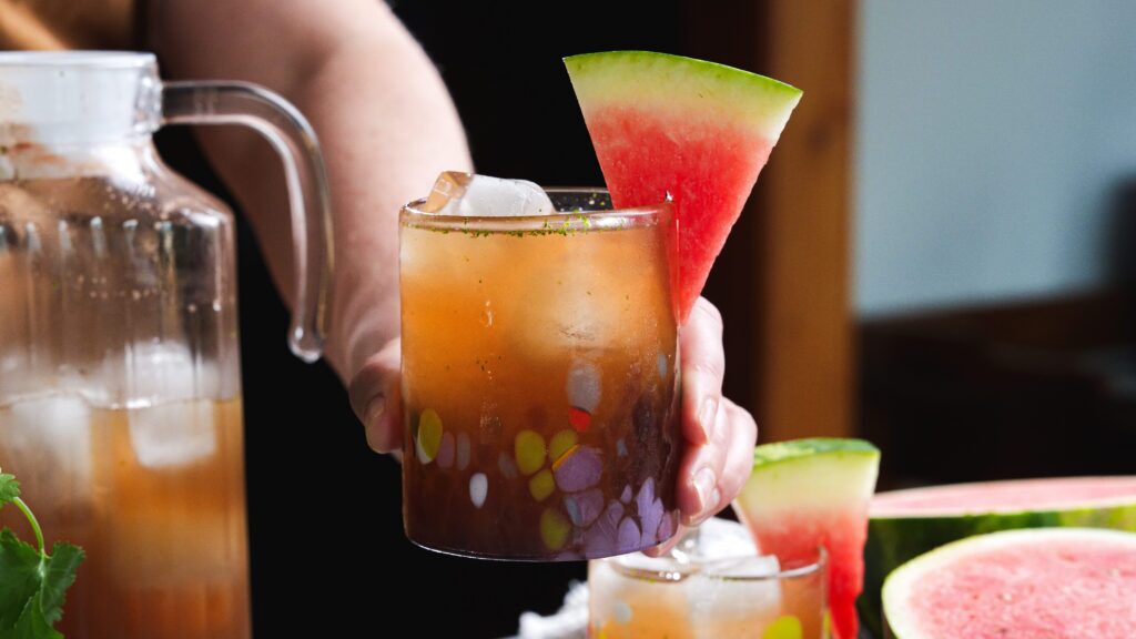 Holding a glass of watermelon agua Fresca.