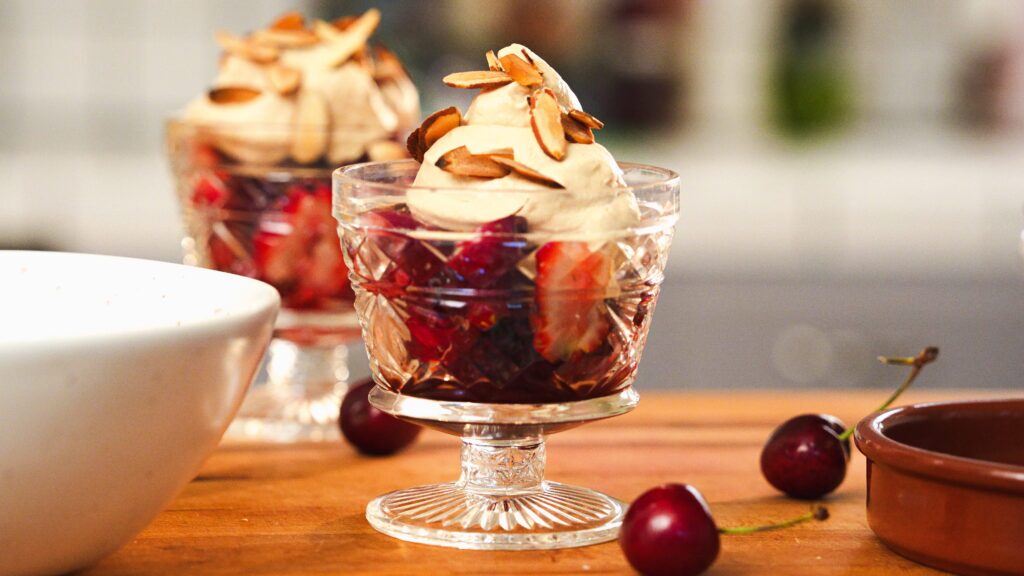 Macerated strawberries and cherries with cream and almonds in parfait glasses.