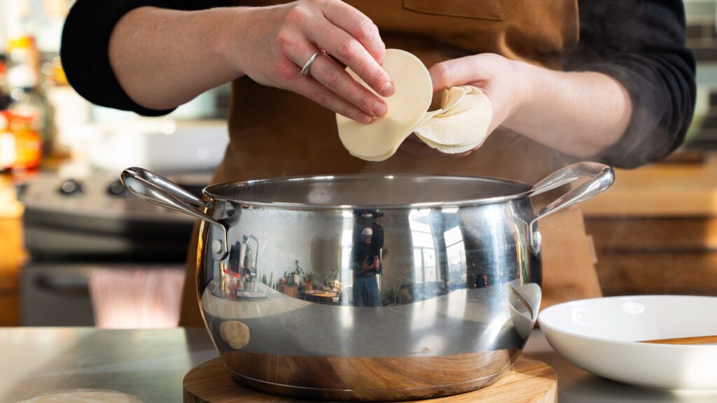 Adding dumpling wrappers to a pot of boiling water to make a pork dumpling recipe.