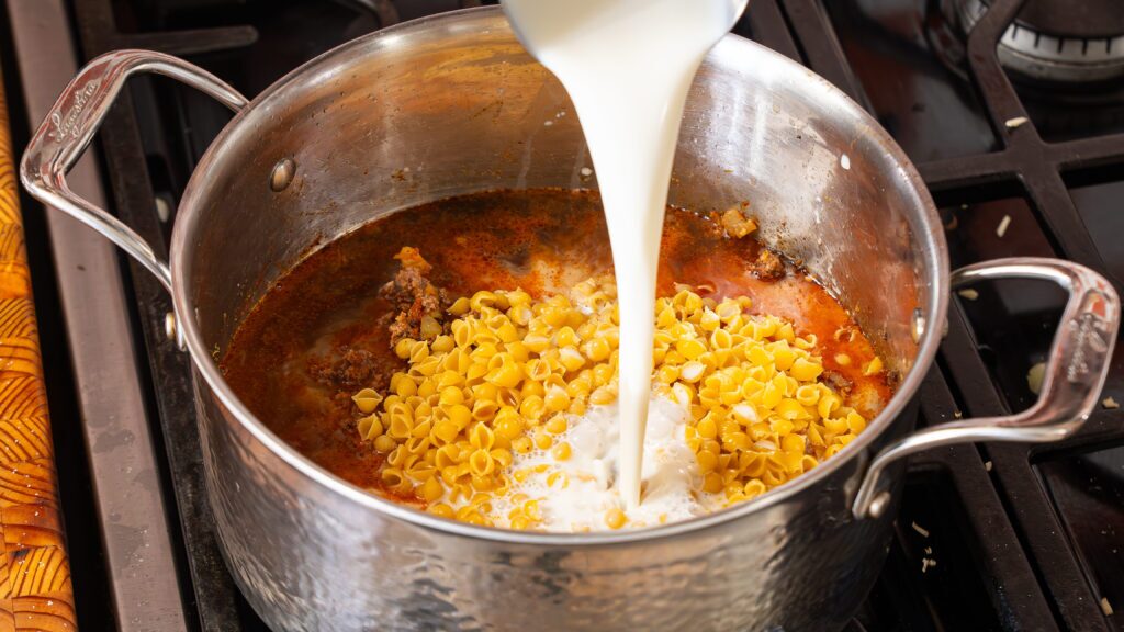 Adding milk and dry pasta to a large pot to make a homemade hamburger helper recipe.