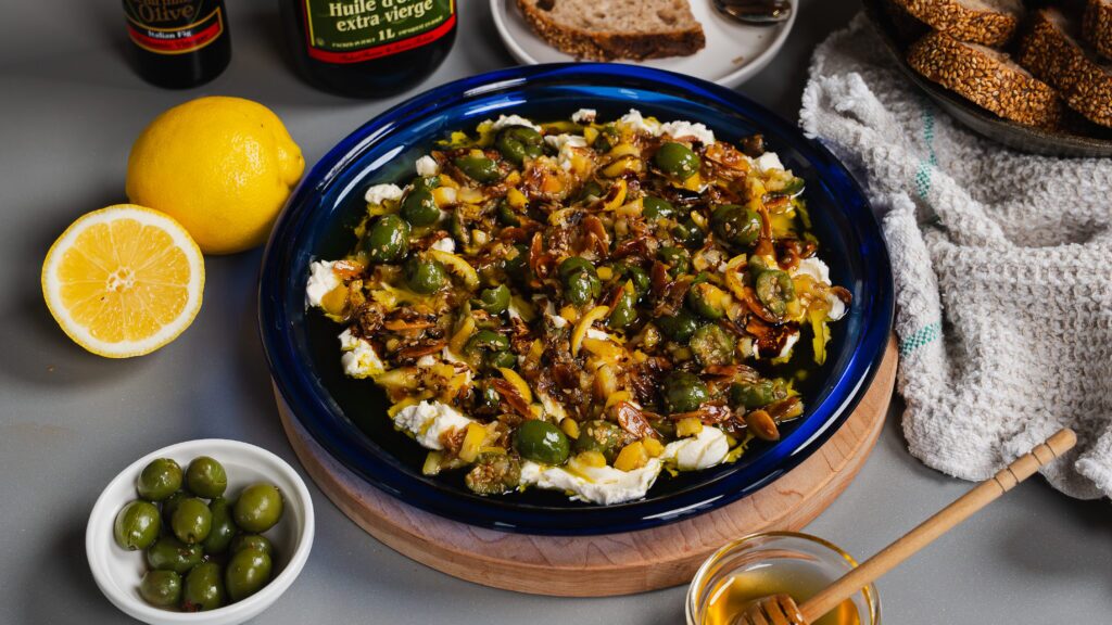 Olive dip with honey & lemon on a blue plate surrounded by ingredients and bread.