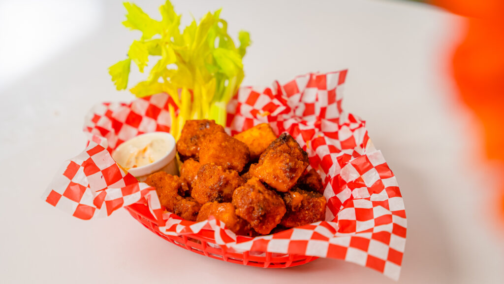 A close up shot of Buffalo Popcorn Tofu in a red basket with a red and white checkered paper.