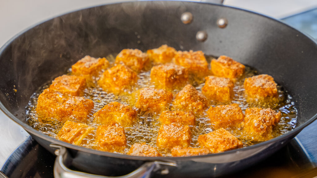 A close up shot of Buffalo Popcorn Tofu frying in a pan. 