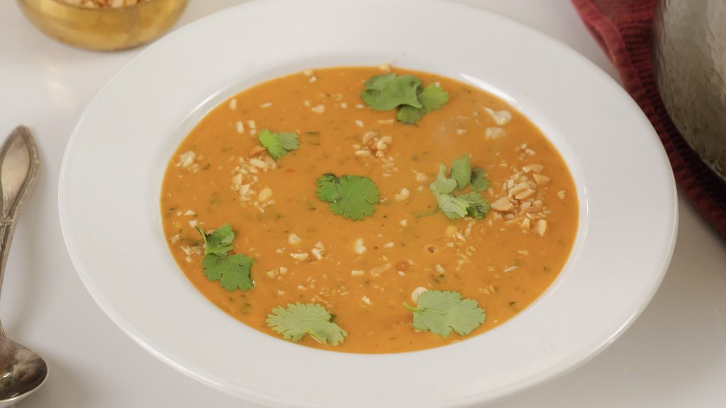 A closer up shot of a bowl of West African Peanut Soup. There are crushed peanuts and fresh cilantro on top. 