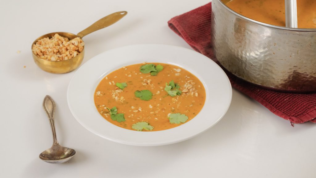 A close up shot of a bowl of West African Peanut Soup. There are crushed peanuts and fresh cilantro on top.