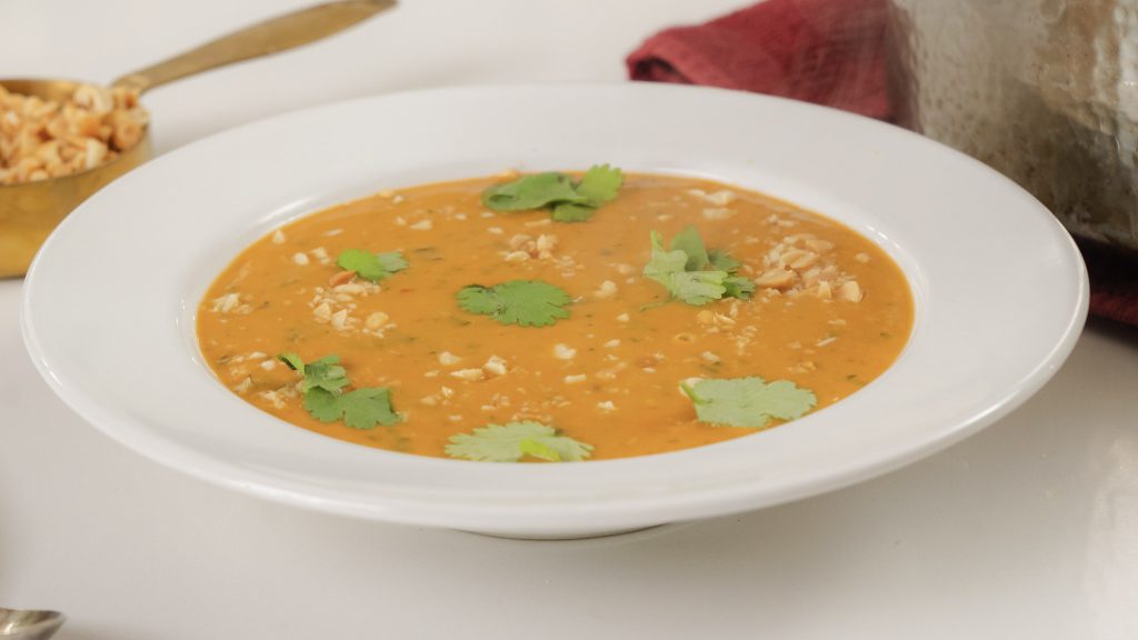 A close up shot of a bowl of West African Peanut Soup. There are crushed peanuts and fresh cilantro on top. 