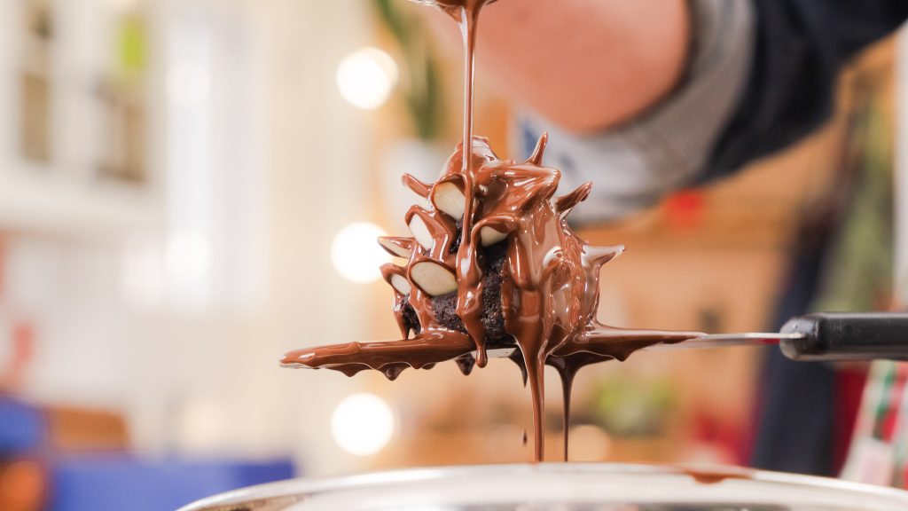 A close up shot of Chocolate Brownie Almond Pinecones being covered in melted chocolate.