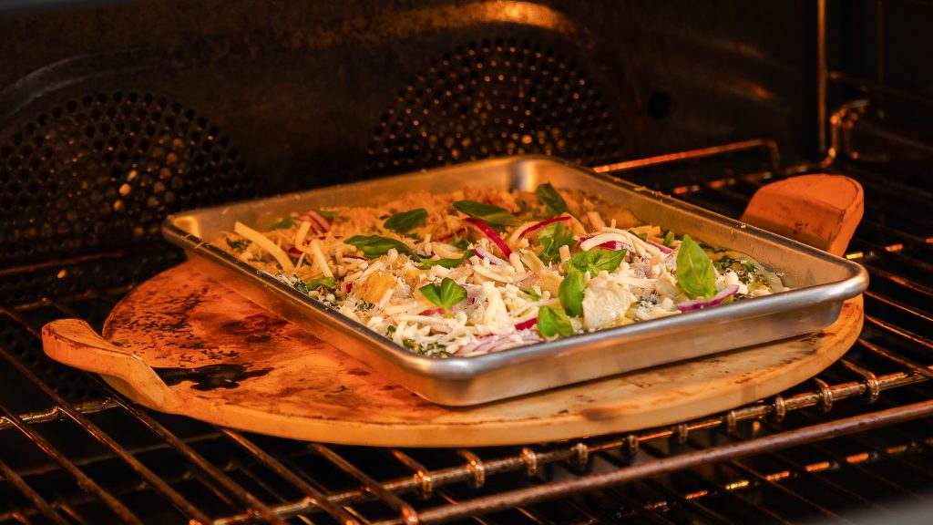 A close up shot of a fully dressed Veggie pizza being placed onto a ripping hot pizza stone. 