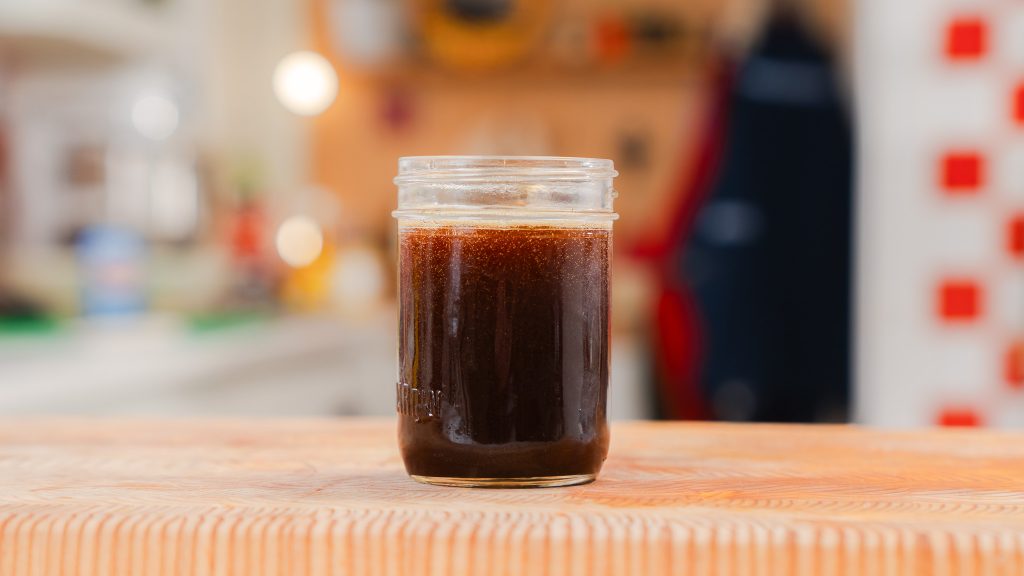 A close up of fairly dark brown butter in a small glass, clear mason jar.