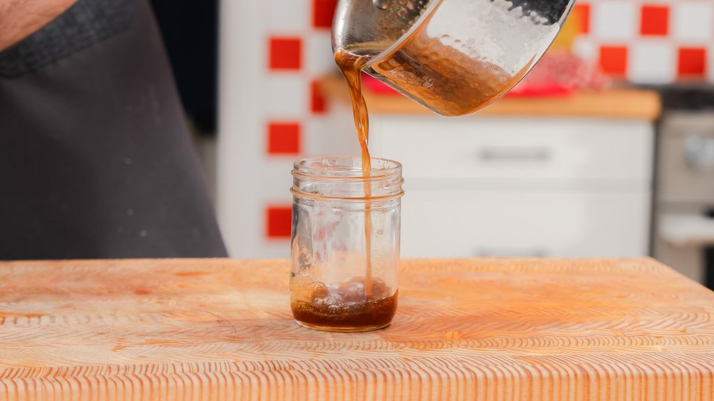 Brown Butter is being poured into a small, clear mason jar. 