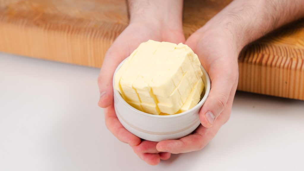 A close up of a person holding a small dish of cubed butter. 