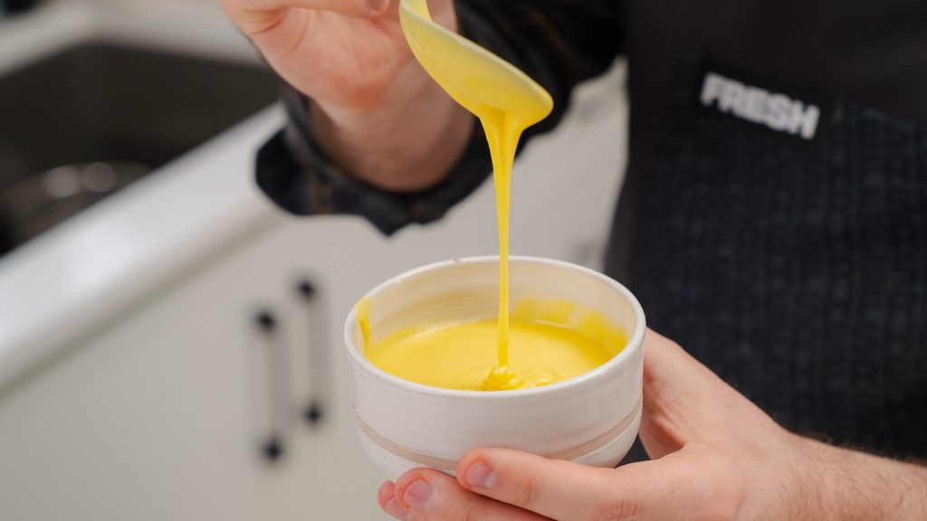 A close up shot of creamy, silky hollandaise sauce falling from a spoon. 