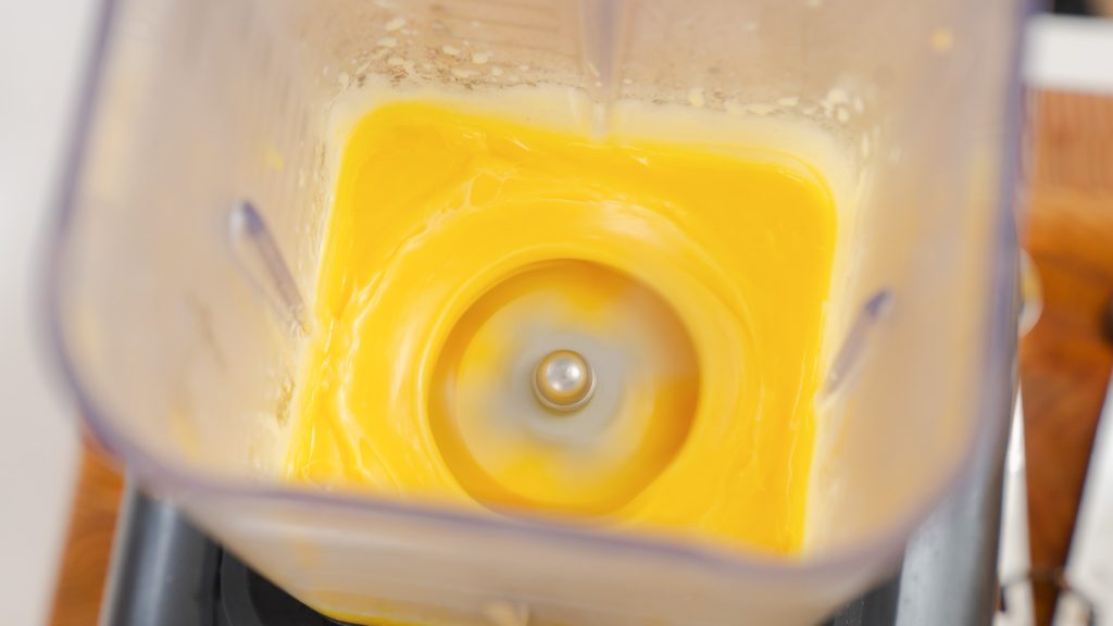 A close up shot of a moving blender with hollandaise sauce being made in it. 