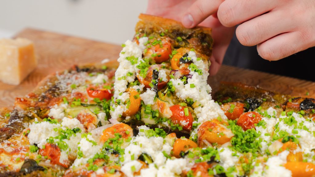 A close up shot of a hand pulling away a slice of veggie pizza.