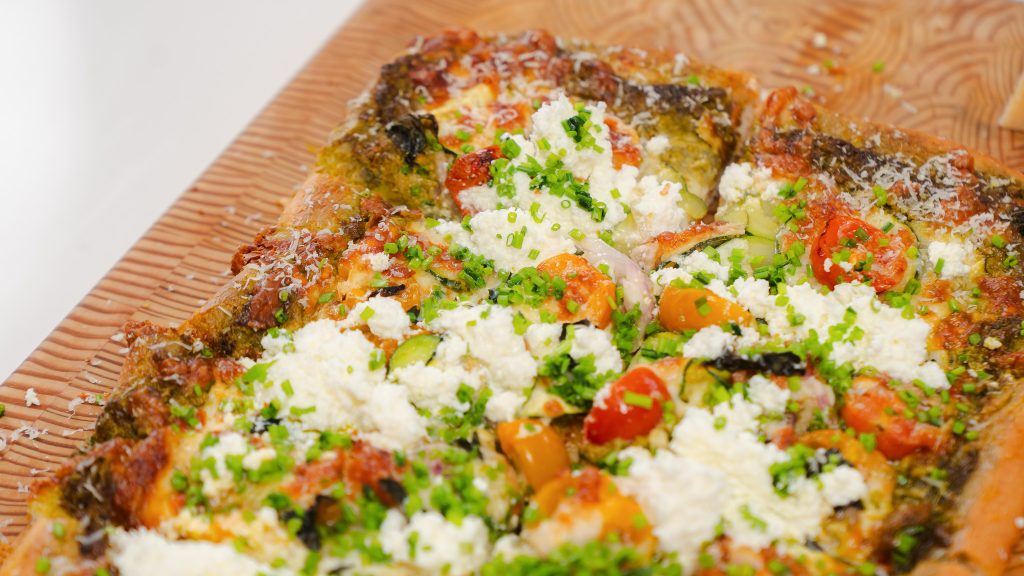 A close up shot of a veggie pizza. Lots of bright colours and golden brown cheese. 