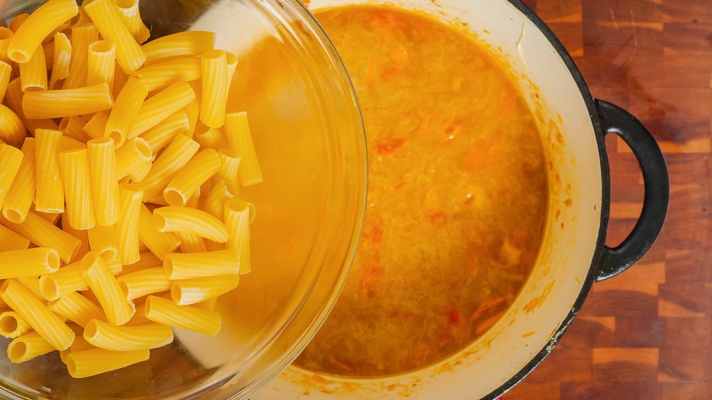 Rigatoni being added to a pot of delicious sauce for a cherry tomato pasta dish.