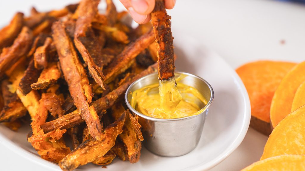 A close up shot of Andy dipping crispy Sweet Potato Fries into a bright yellow curry mayo.