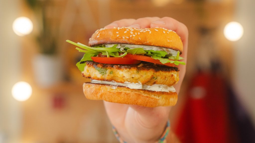 A close up shot of a hand holding a fully dressed chickpea Burger. 