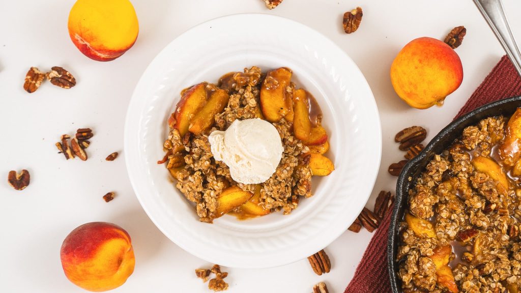 peach crisp in white bowl with ice cream scoop