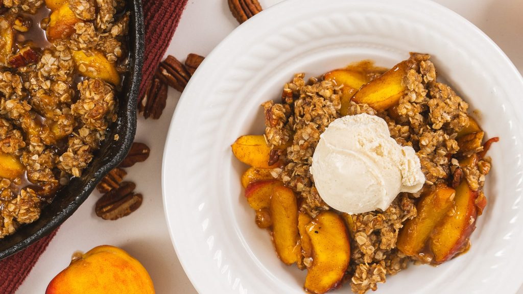 close shot of ice cream melting over peach pecan crumble